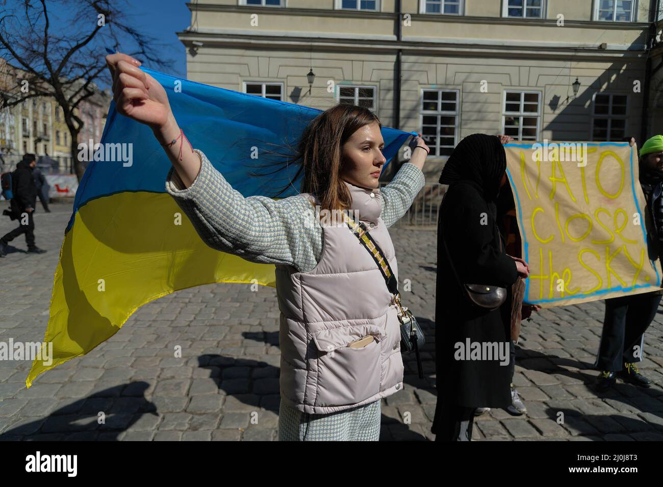 Une femme porte le drapeau ukrainien lors d'un rassemblement en faveur de Marioupol et appelle l'OTAN à fermer les cieux au-dessus de l'Ukraine. Pendant trois semaines, l'avant-poste est de l'Ukraine - Marioupol est en état de siège. Chaque jour, les Ukrainiens meurent dans la ville, en particulier les enfants ukrainiens. Les racistes n'épargnent pas les vivants ou les enfants à naître, ils ne permettent pas aux morts d'être enterrés avec dignité. Les bombardements ennemis ont presque détruit une grande ville d'un demi-million, et le siège a conduit à une catastrophe humanitaire. Marioupol a été défendue héroïquement par le Régiment Azov, les Forces armées et le Service de sécurité nationale Banque D'Images