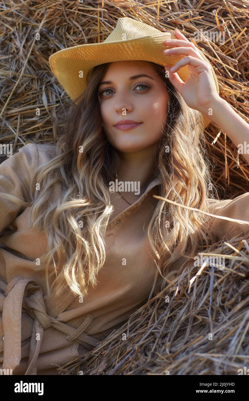 Jeune femme blonde dans une combinaison beige est assise sur les rouleaux de foin. Banque D'Images