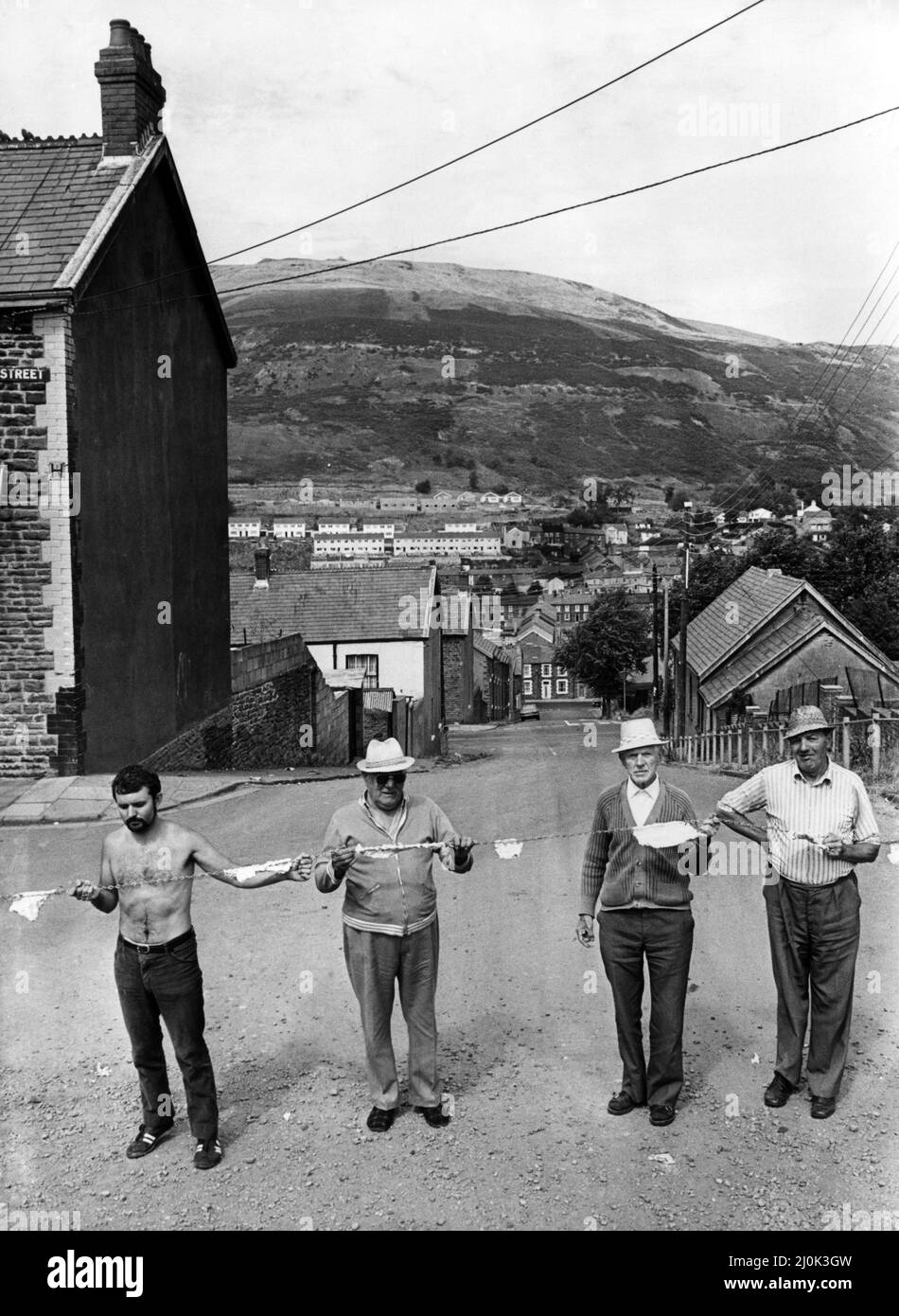 Les habitants de King Street, Gelli, ont placé une chaîne en travers d'une voie près de leurs maisons pour empêcher les camions de prendre une courte coupe jusqu'à un bout près de leurs maisons. Sur la photo, quatre des résidents avec la chaîne Raven Hill à l'arrière-plan que les camions utilisent comme raccourci. Gelli est un village de la vallée de Rhondda Fawr, dans le quartier de Rhondda Cynon Taff, pays de Galles. La vue de Alexander Road, photographiée en arrière-plan dans une pointe de charbon. 13th août 1981. Banque D'Images