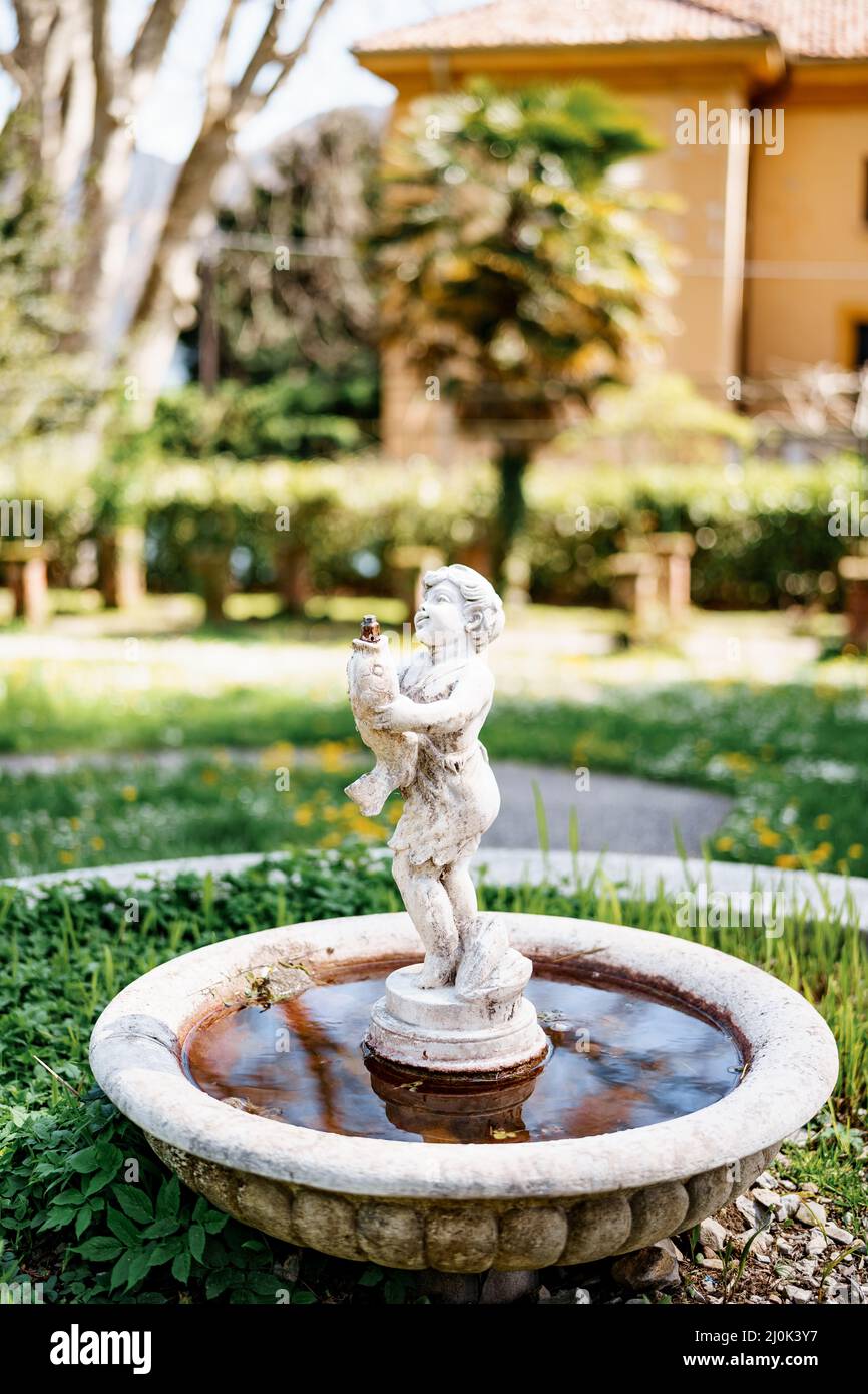 Une petite fontaine de jardin sous la forme d'une figurine d'un enfant avec un poisson entre ses mains dans la cour. Banque D'Images