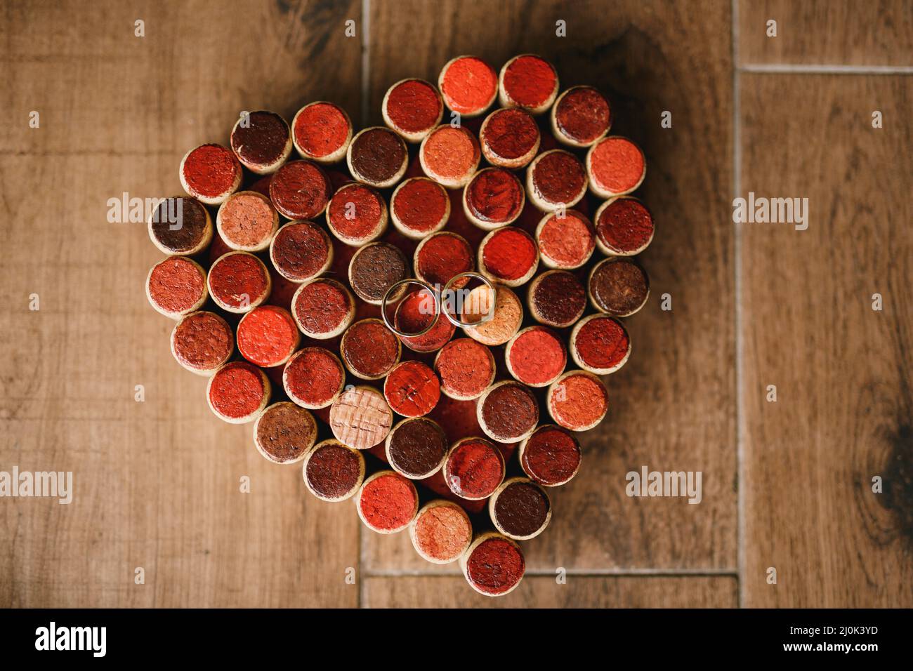 Anneaux de mariage de la mariée et du marié sur un motif de coeurs faits de bouchons de bouteille de vin sur une texture en bois. Banque D'Images