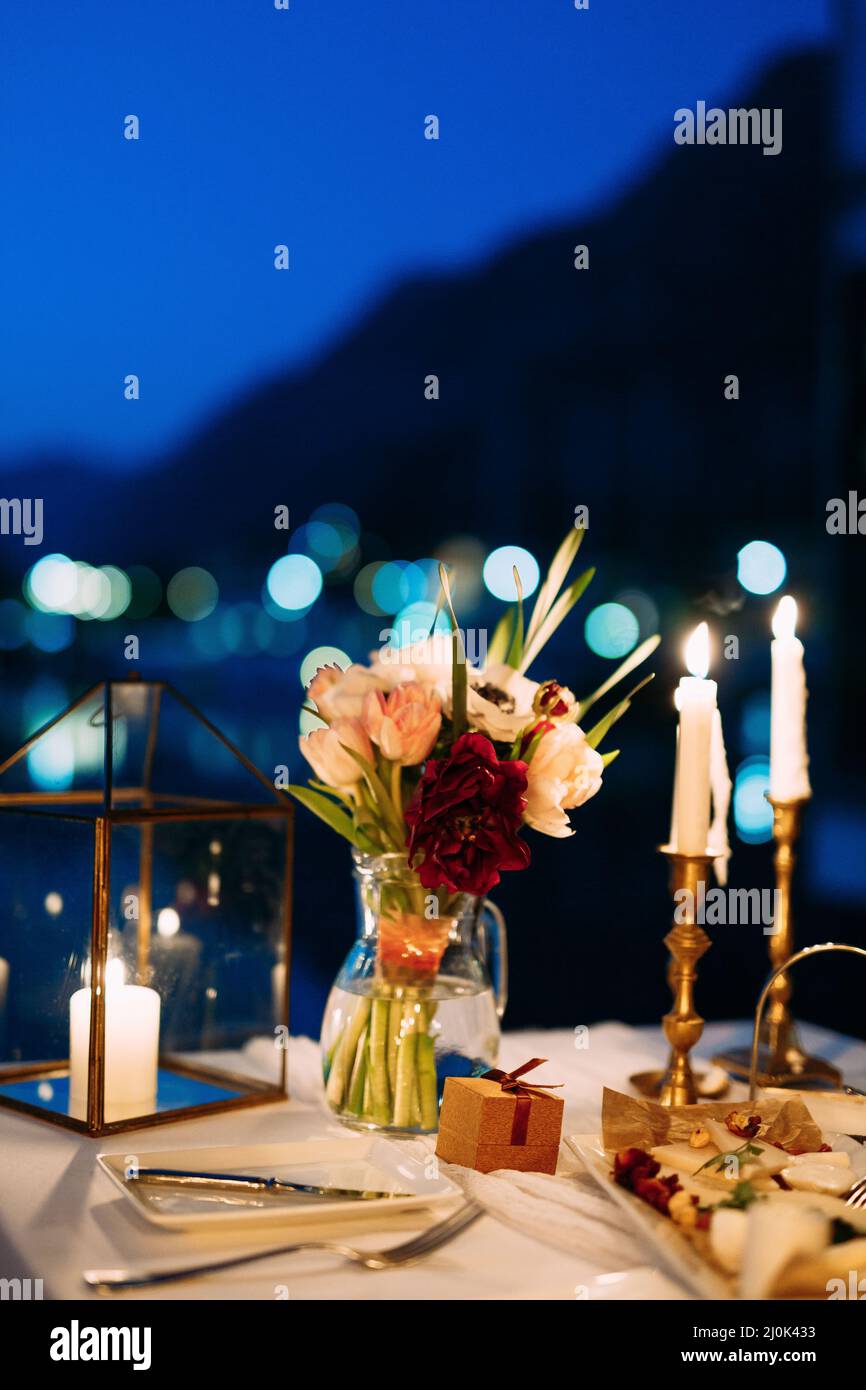Réception de table de dîner de mariage. Un bouquet de fleurs dans un vase en verre sur la table la nuit. Les bougies blanches en chandeliers expirent Banque D'Images