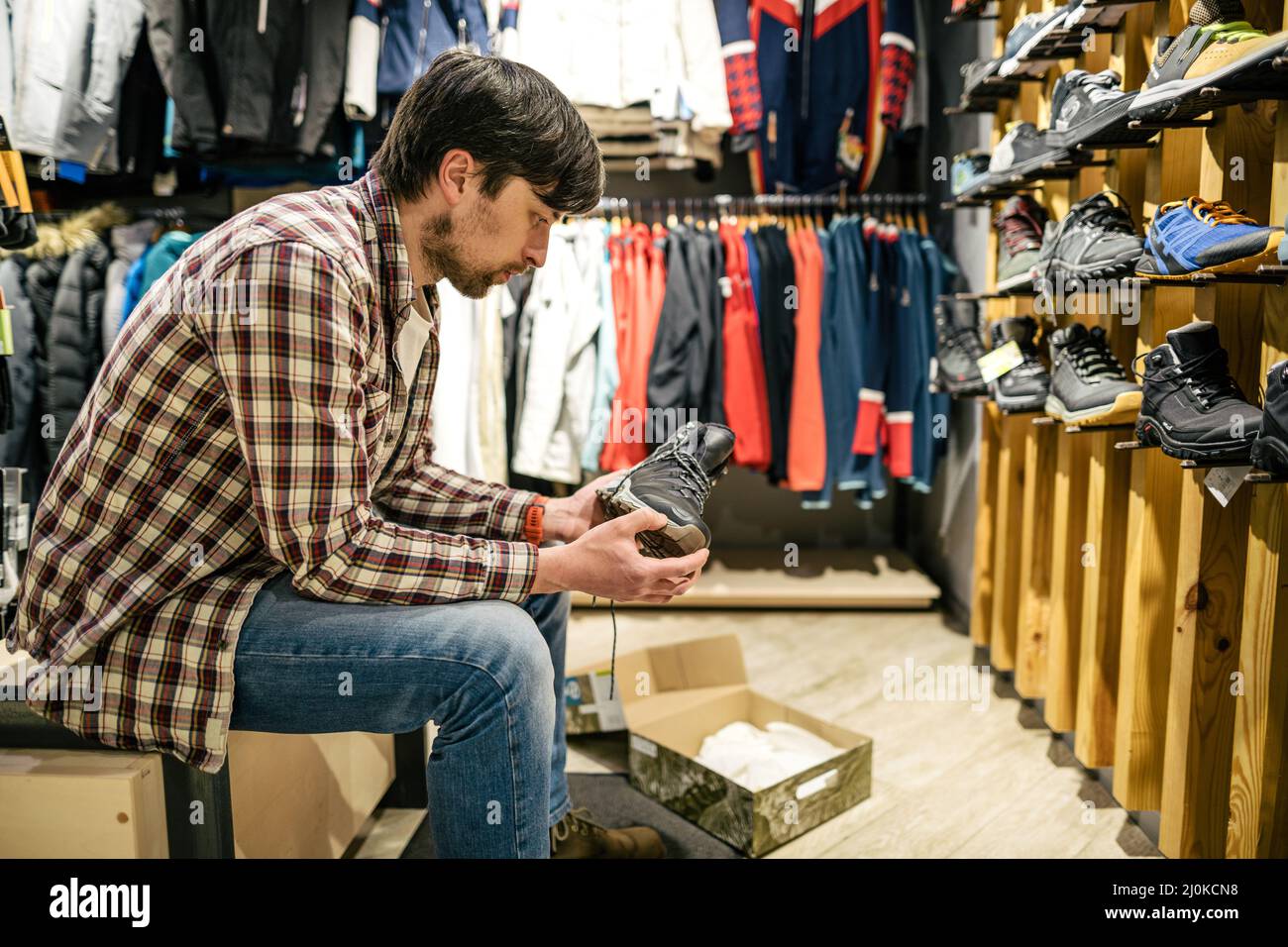 L'homme caucasien tient et examine des bottes de randonnée avant d'acheter dans une boutique pour le tourisme et le sport. Le client évalue la qualité de Banque D'Images