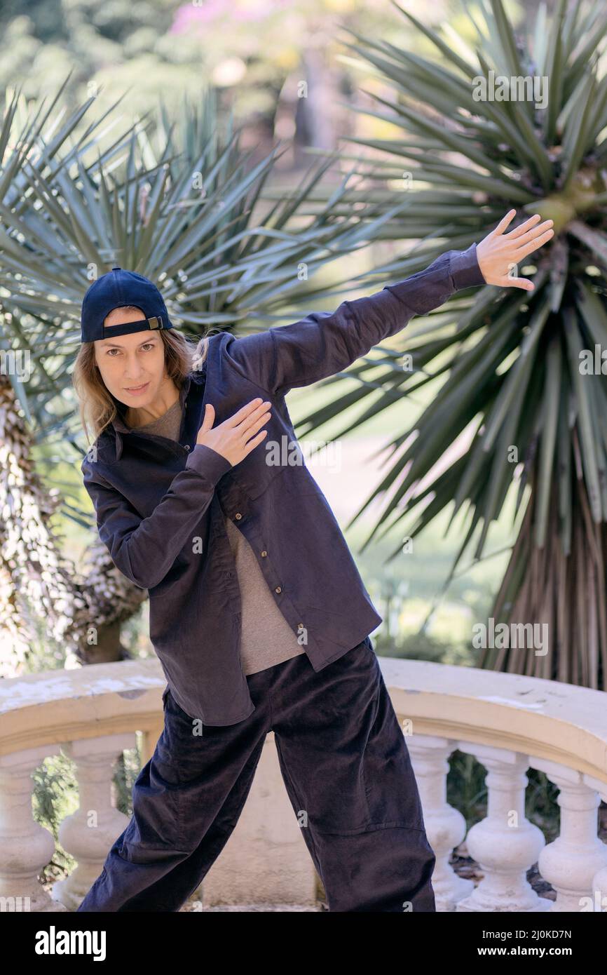 Une jeune femme habillée de style hip-hop se dresse dans une pose dans le parc, sur fond de palmiers Banque D'Images