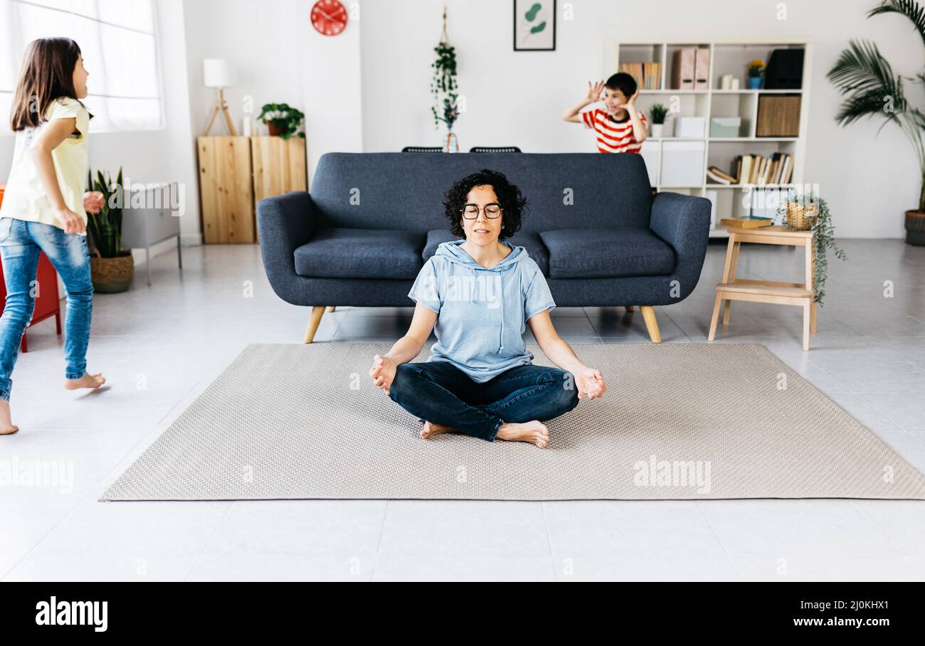 Des enfants enthousiastes jouant autour de mère paisible faisant du yoga dans le salon Banque D'Images