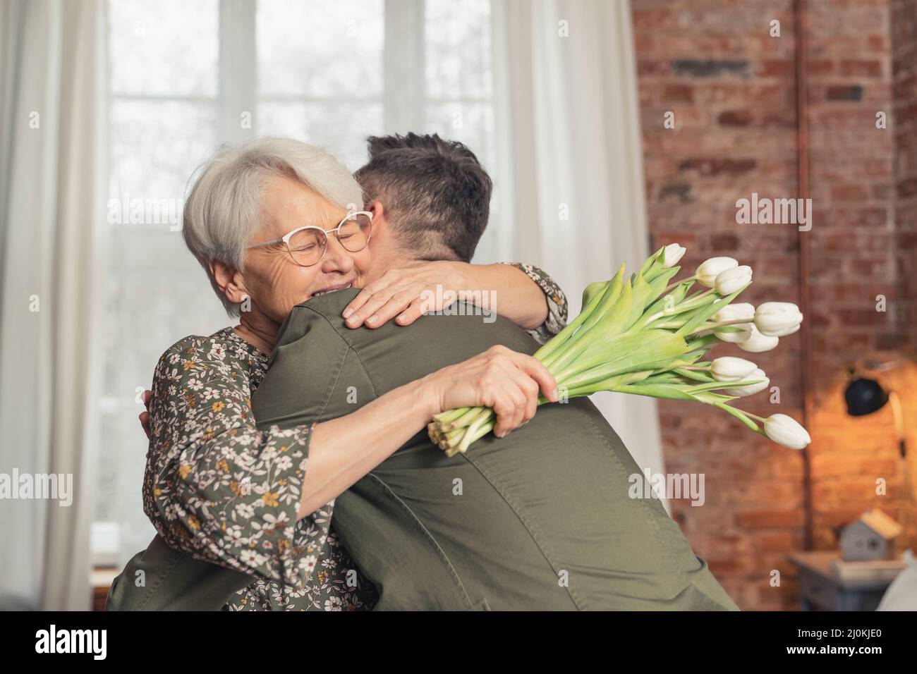 embrassez-vous entre la jeune femme âgée ravie dans ses 70s ans et son fils adulte qui lui a donné des fleurs blanches. Photo de haute qualité Banque D'Images