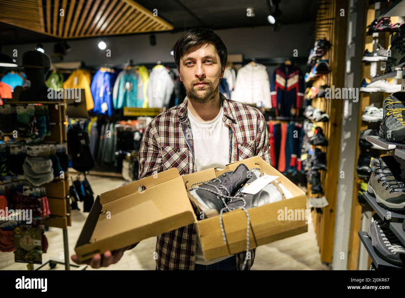 Conseiller commercial mâle caucasien dans un magasin extérieur présentant des bottes de randonnée à l'acheteur. Un vendeur dans un magasin de sport aide un sh Banque D'Images