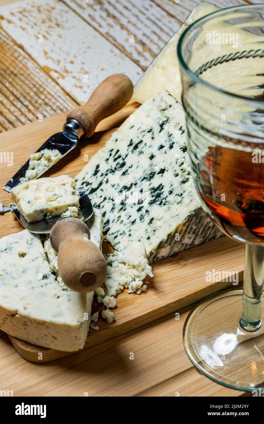 Fromages bleus tranchés et tranchés avec couteaux à fromage et verres de vin de Claret espagnol sur des planches de bambou et une table en bois Banque D'Images