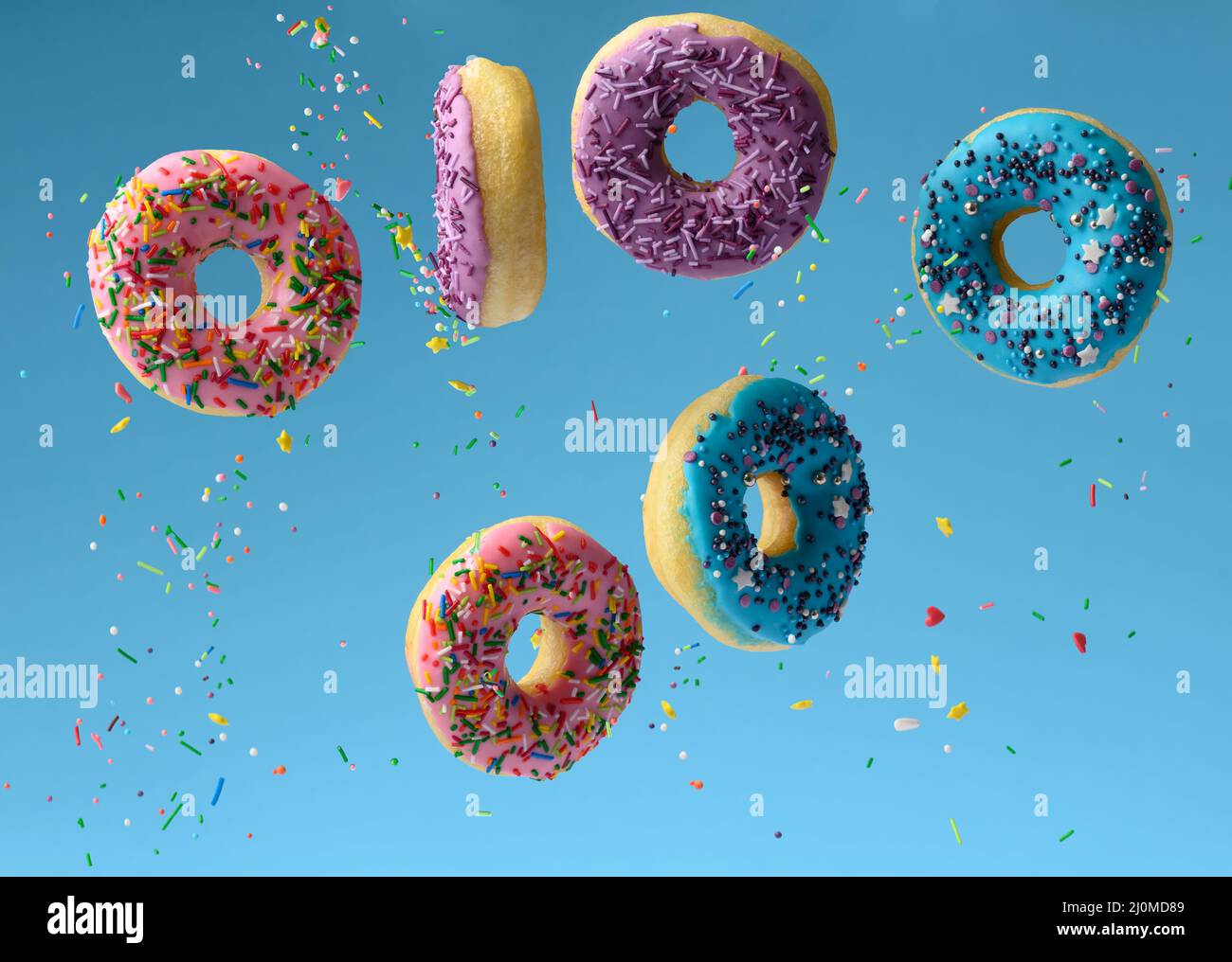 Les beignets multicolores doux levent sur fond bleu, les saupoudrés de sucre volent autour Banque D'Images