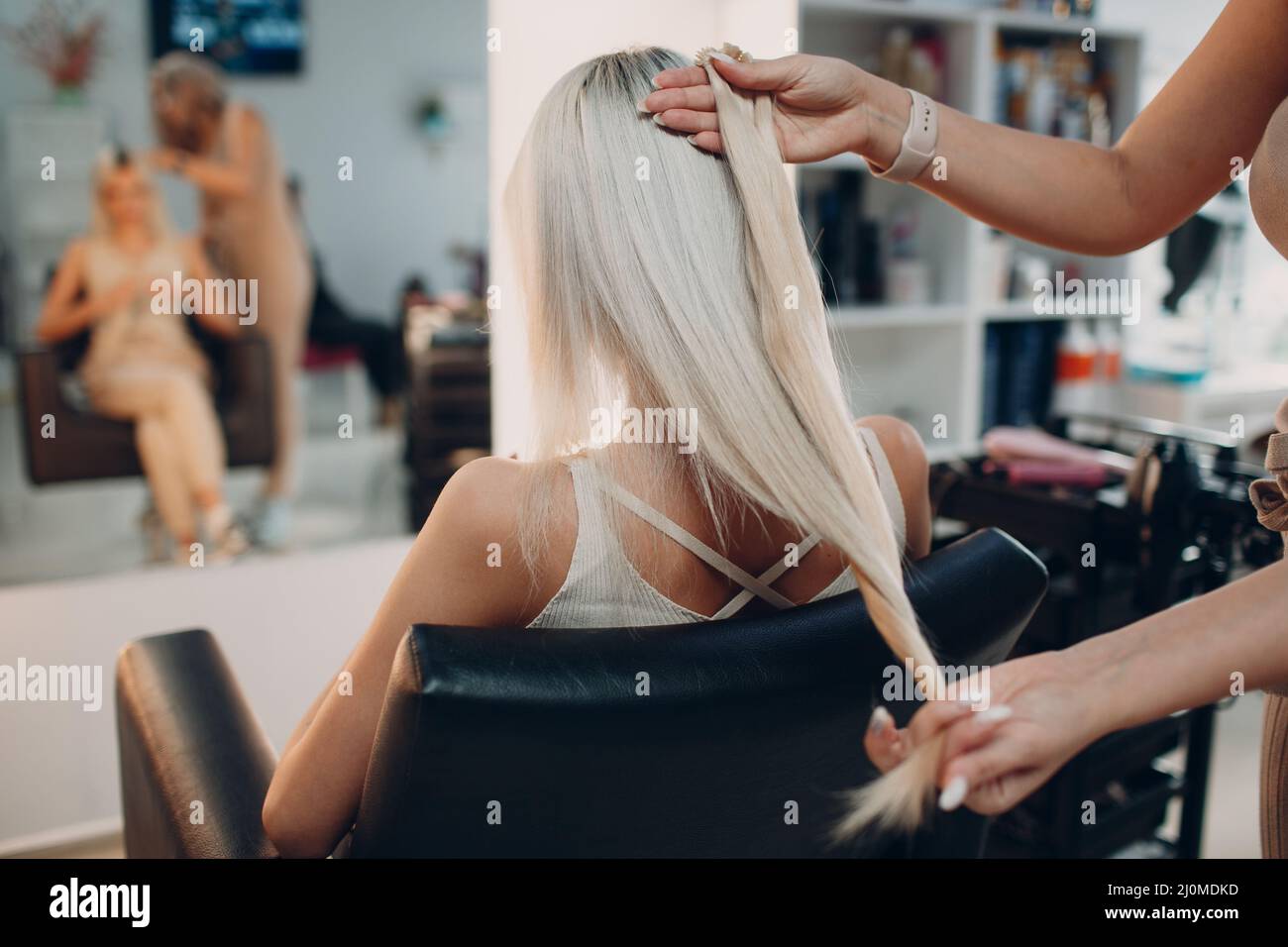 Coiffeur femme faisant des extensions de cheveux à la jeune femme avec des cheveux blonds dans le salon de beauté. Rallonge de cheveux professionnelle. Banque D'Images