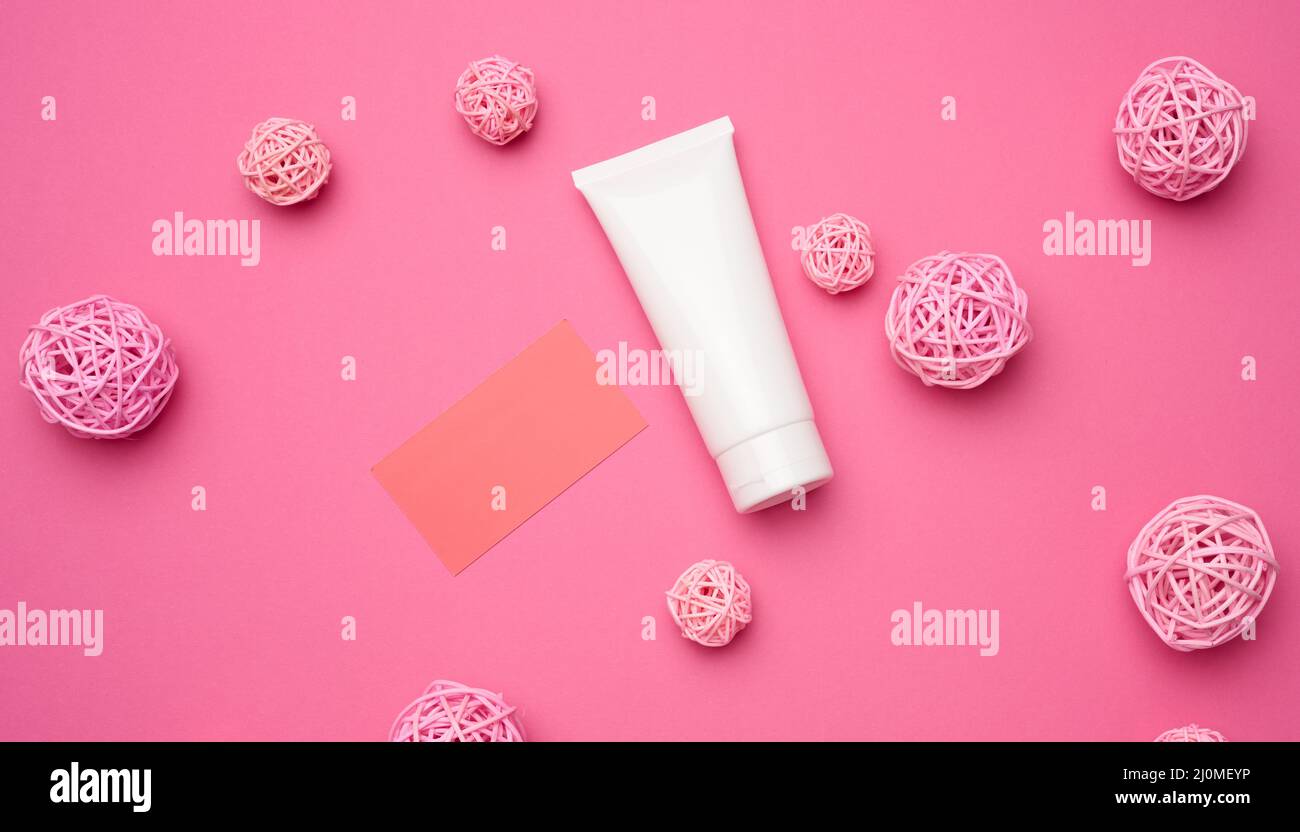 Carte papier et tubes en plastique blanc vides pour cosmétiques sur fond rose. Emballage pour crème, gel, sérum, publicité et rp Banque D'Images