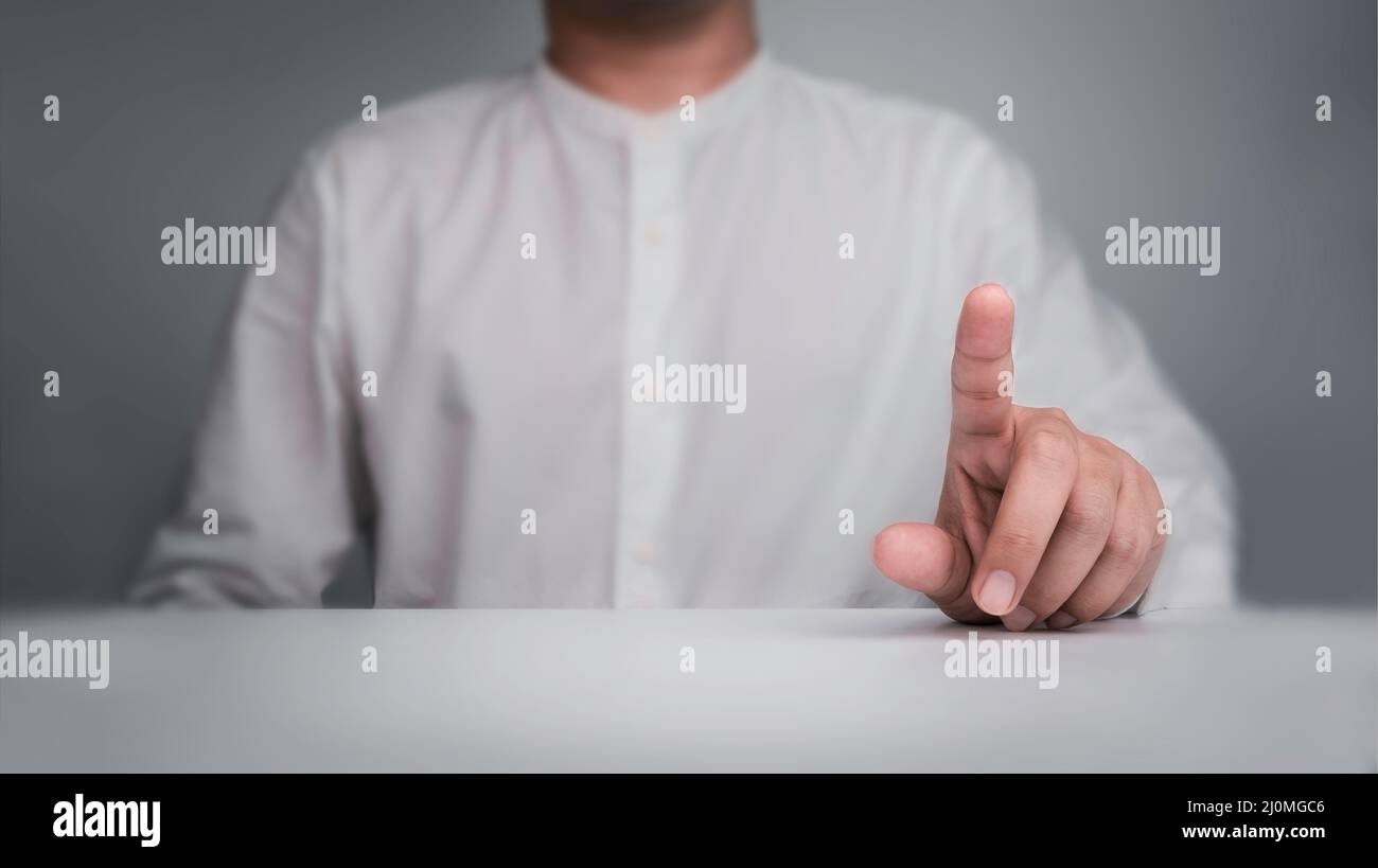Toucher l'écran tactile virtuel geste d'un professionnel en chemise blanche, assis derrière la table blanche sur fond gris. Pointez la main ou appuyez sur Banque D'Images