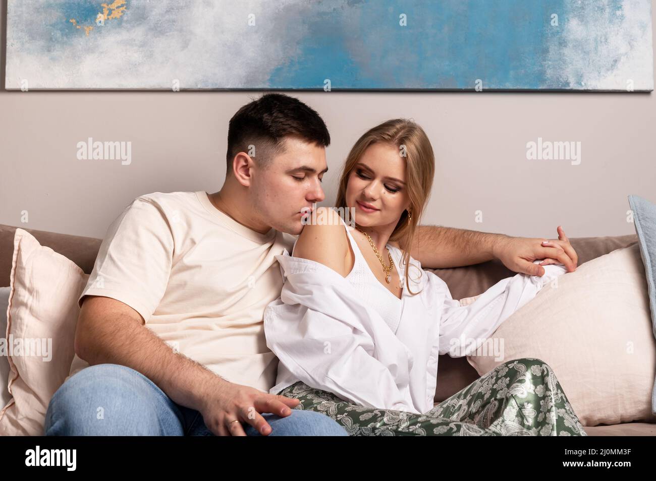 Couple heureux assis sur un canapé à la maison. Beau homme embrassant belle femme sur l'épaule avec tendresse et amour. Concept de la date du domicile. Photo de haute qualité Banque D'Images