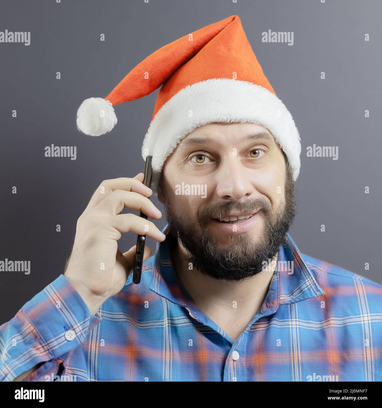 Un homme barbu dans un chapeau de père Noël a mis son téléphone cellulaire à son oreille. Vœux de vacances à vos proches Banque D'Images