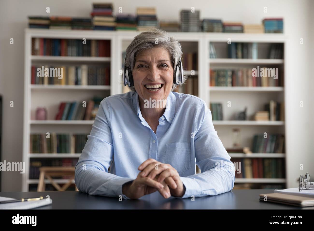 Une femme plus âgée, dans un casque, regardant la caméra, peut profiter de la visioconférence Banque D'Images