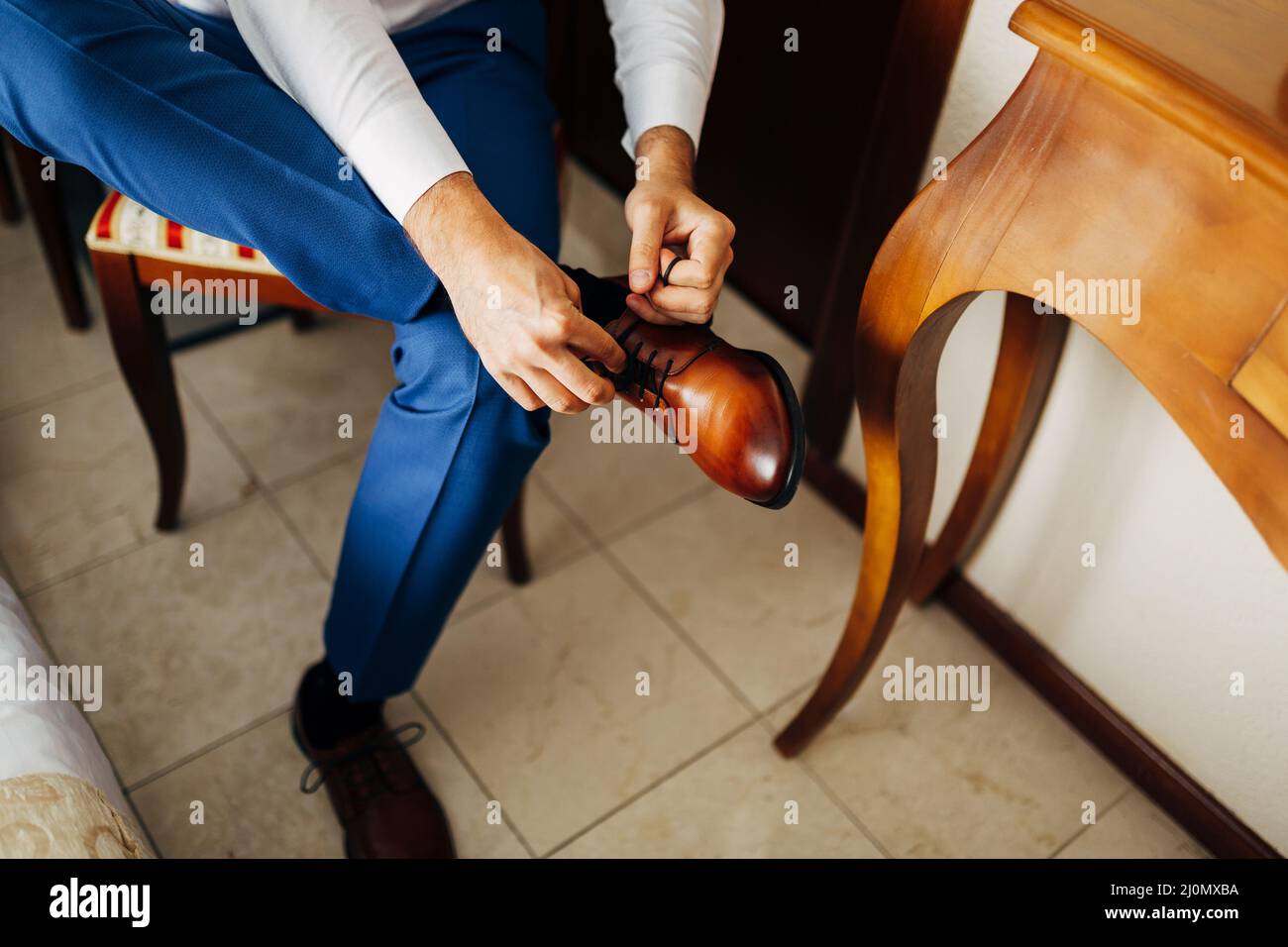 Homme dans une chemise blanche et pantalon bleu attache ses bottes, assis sur une chaise.Gros plan Banque D'Images