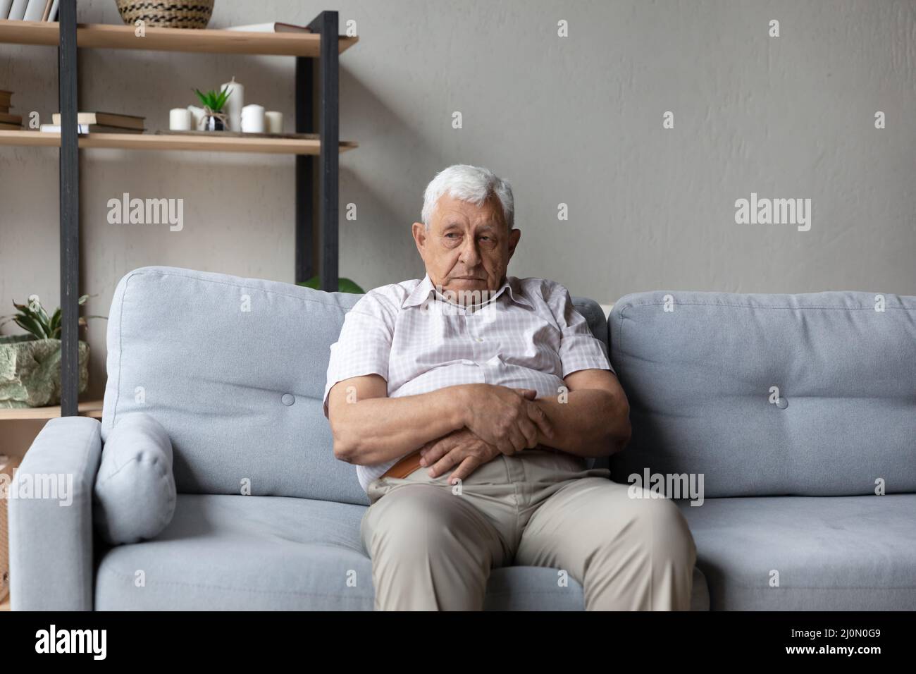 Un vieil homme attentionné s'assoit seul sur un canapé perdu dans ses pensées Banque D'Images