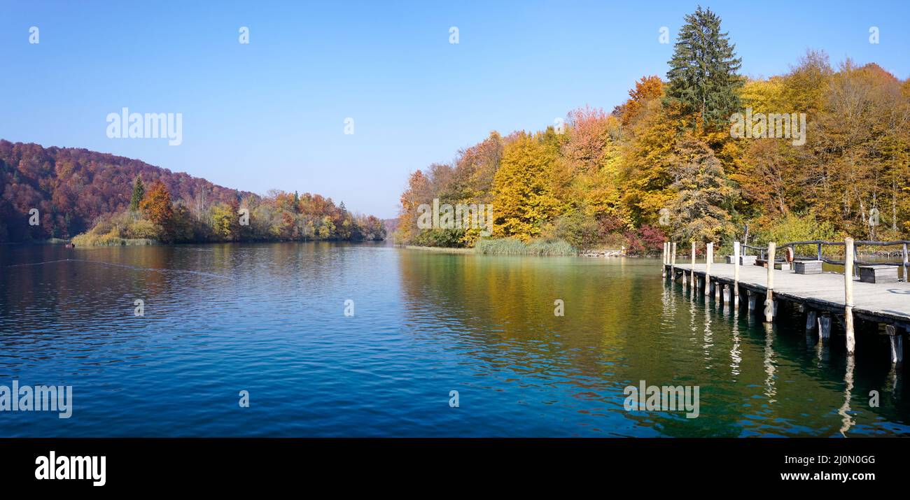 Vue horizontale sur le lac calme avec une chute d'eau et un feuillage d'automne coloré et un quai au premier plan Banque D'Images