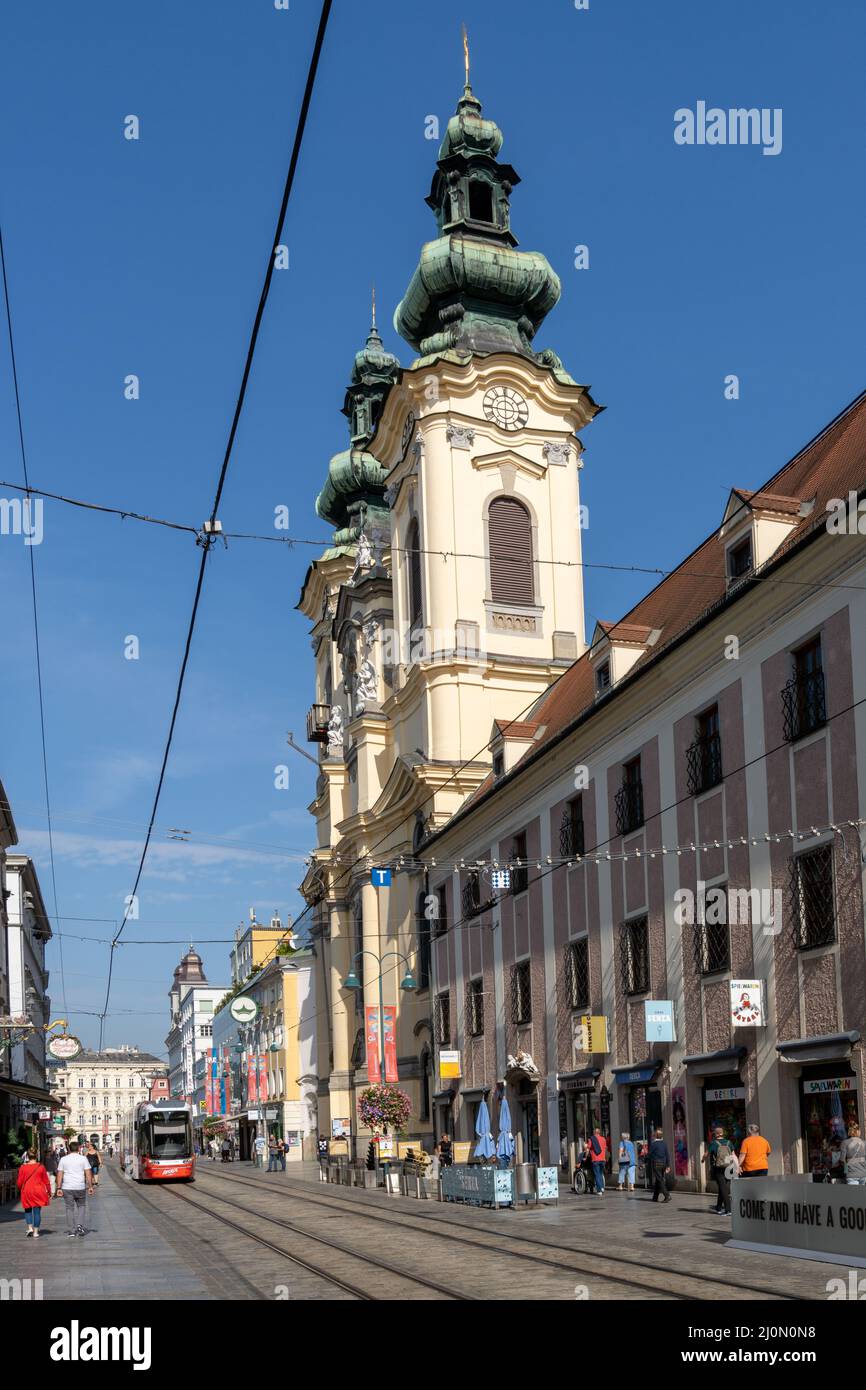 Vieille ville de Linz avec des trams colorés passant devant une église historique Banque D'Images