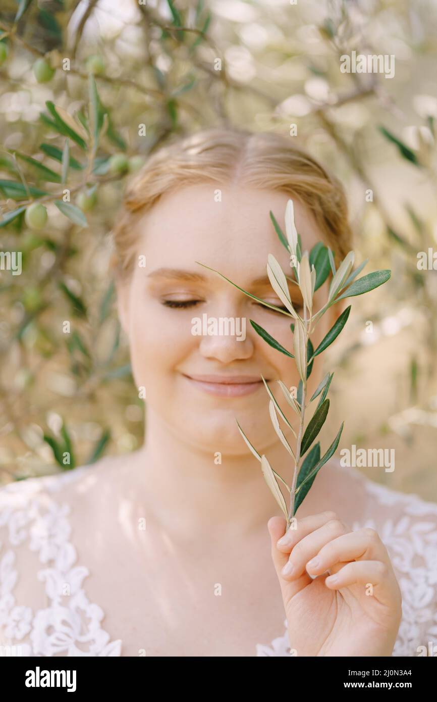 La mariée souriante se tient avec les yeux fermés et la branche d'olive à la main Banque D'Images