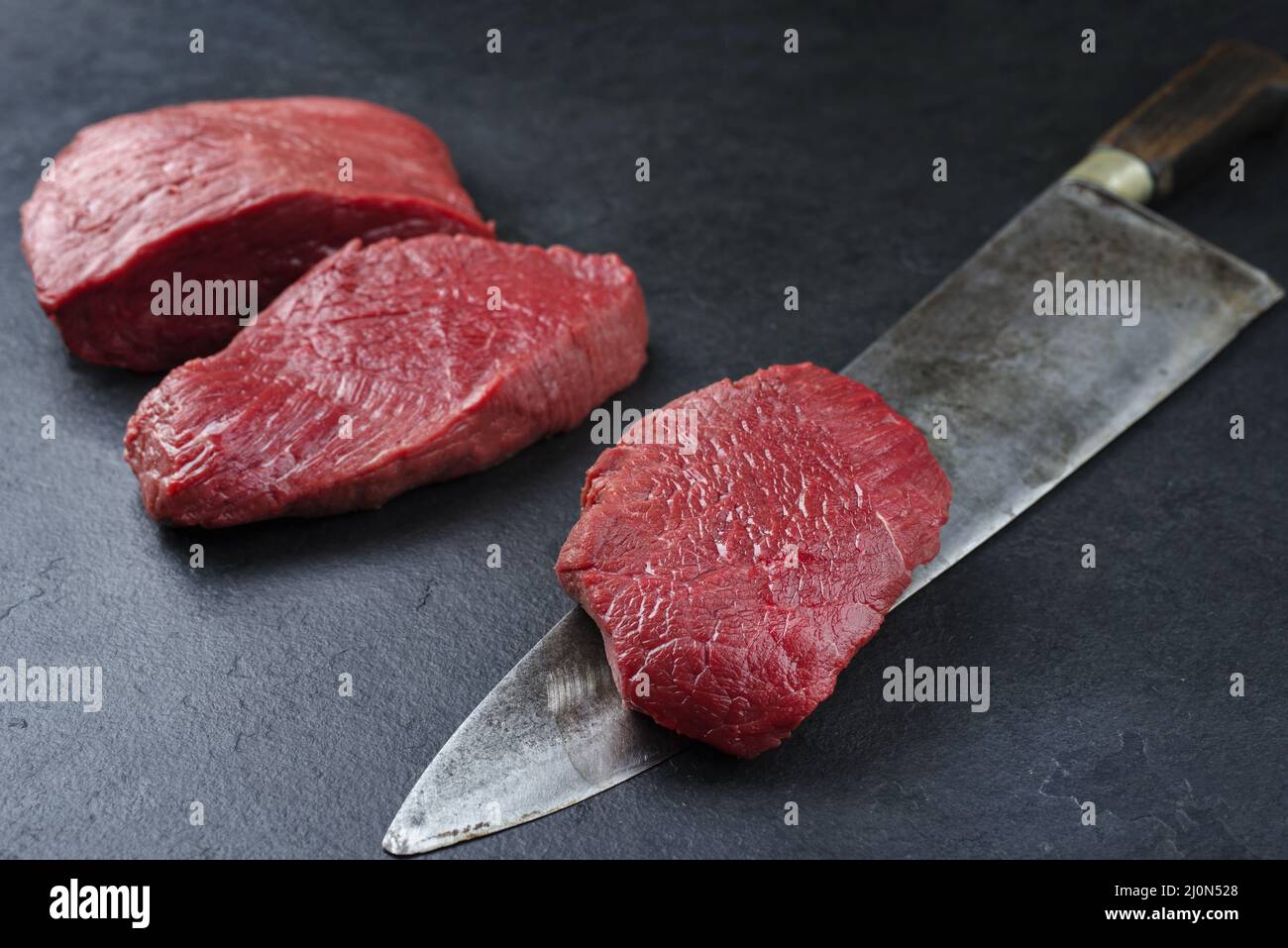Morceau de steak et tranches de bœuf de bison vieilli et sec brut offert en gros plan sur fond noir avec espace de copie Banque D'Images