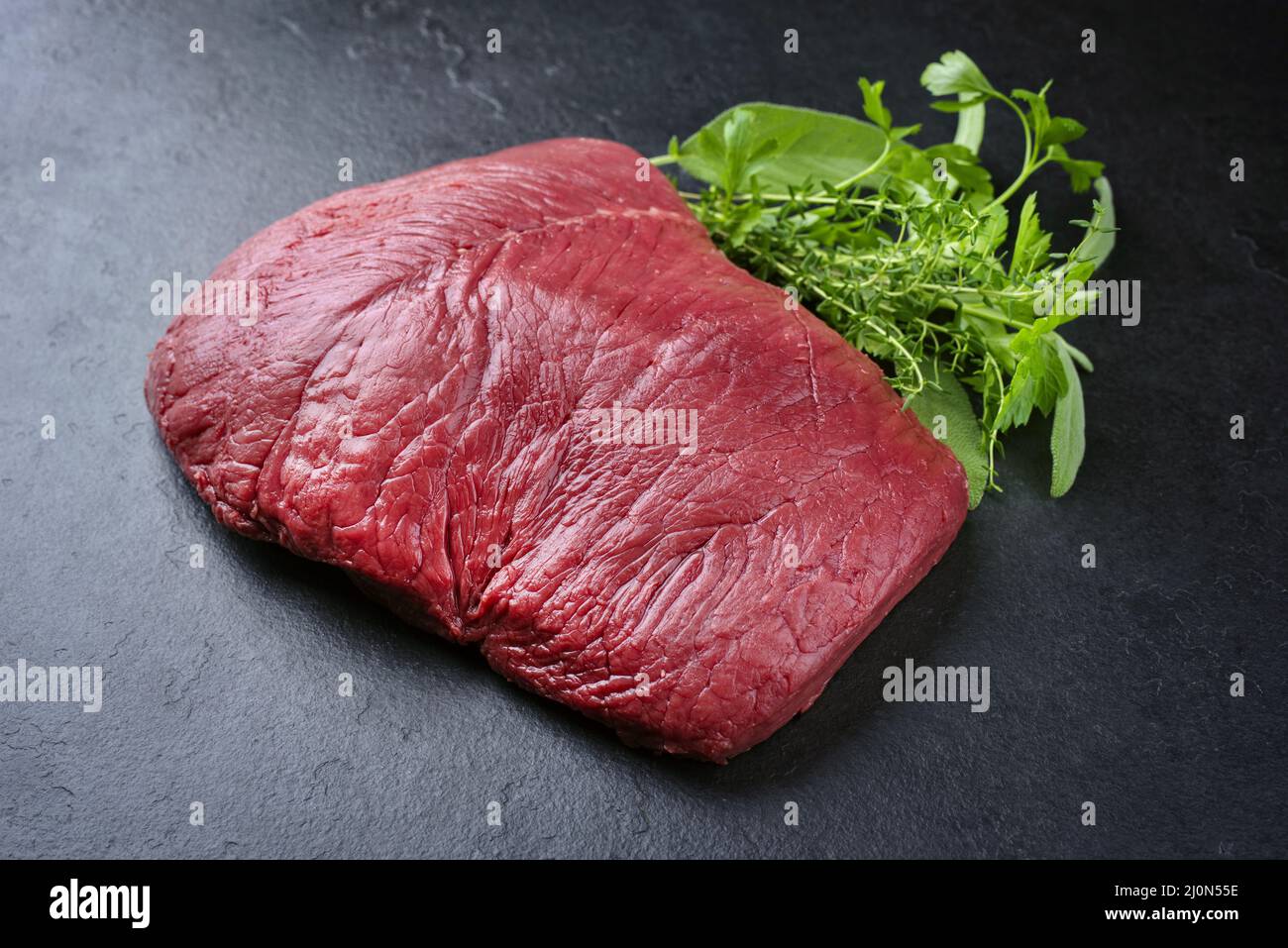 Morceau de steak de bœuf de bison vieilli et sec brut en gros plan avec des herbes sur fond noir avec espace de copie Banque D'Images