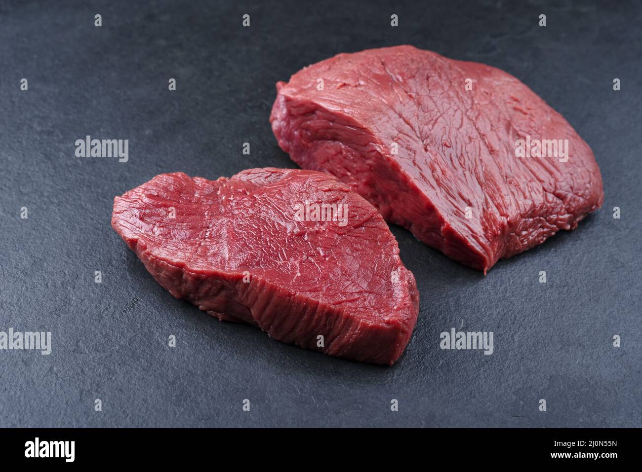 Morceau de steak et tranches de bœuf de bison vieilli et sec brut offert en gros plan sur fond noir avec espace de copie Banque D'Images
