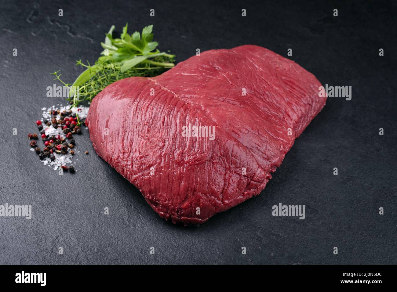 Morceau de steak de bœuf de bison vieilli et sec brut en gros plan avec des herbes et épice sur fond noir avec espace de copie Banque D'Images