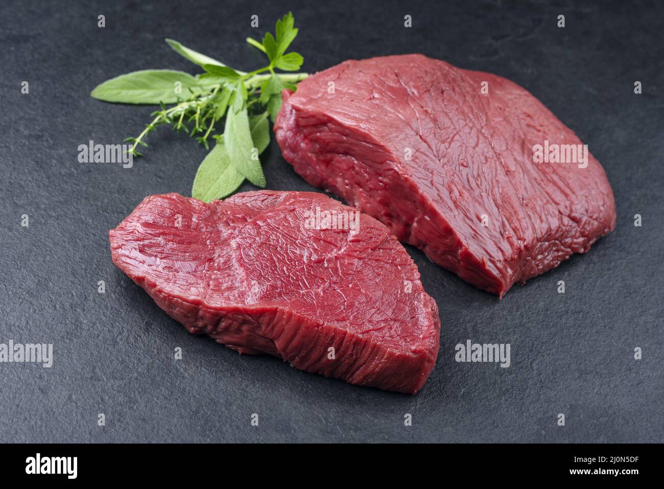 Morceau de steak de bosse de bœuf de bison sec et sec et tranches d'herbes offertes en gros plan sur fond noir Banque D'Images