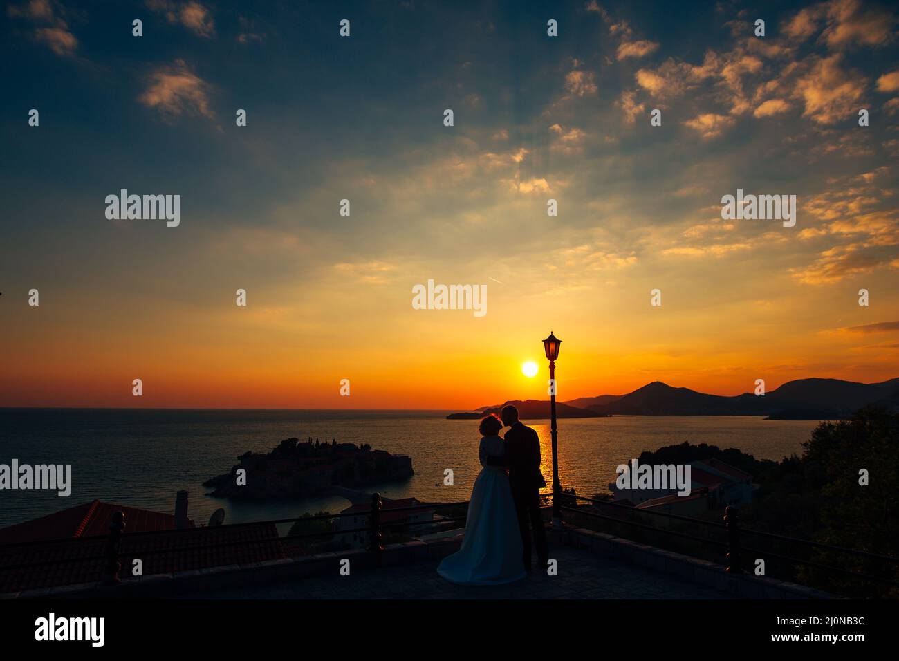 Les jeunes mariés se tiennent sur une terrasse d'observation surplombant l'île de Sveti Stefan, près de Budva, au Monténégro, au coucher du soleil Banque D'Images