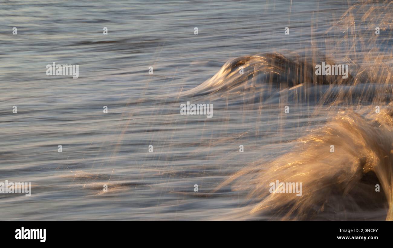 Les vagues de l'océan s'écrasant sur les rochers de la plage, l'eau étincelante tombe au lever du soleil Banque D'Images