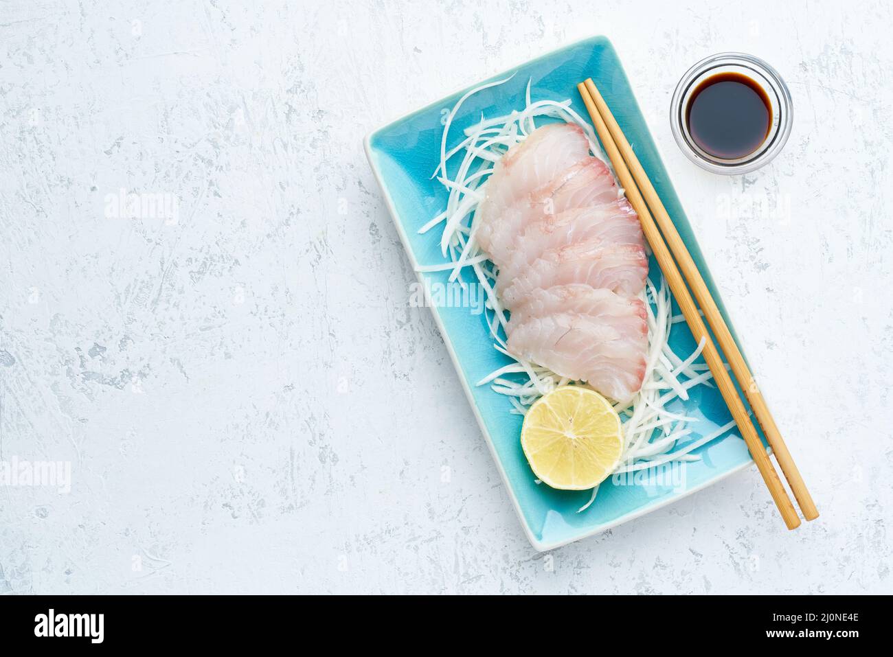 Sashimi à partir de tranches de filet de poisson blanc brut sur une plaque bleue sur fond blanc. Banque D'Images