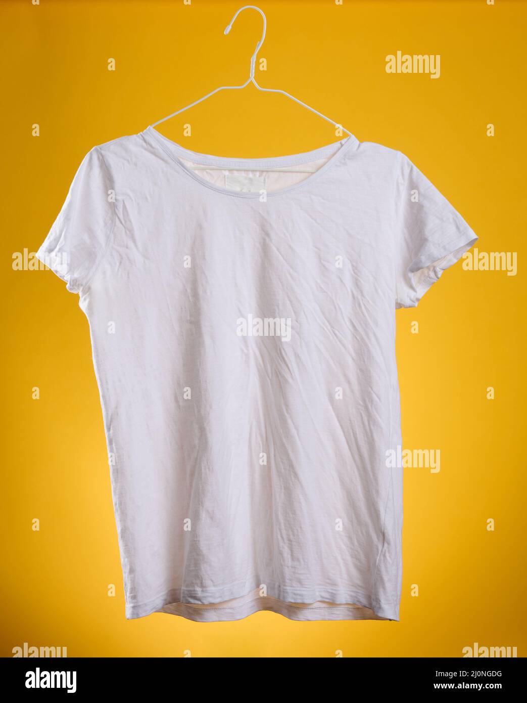 T-shirt en coton blanc froissé accroché à un cintre sur fond jaune, vêtements d'été Banque D'Images