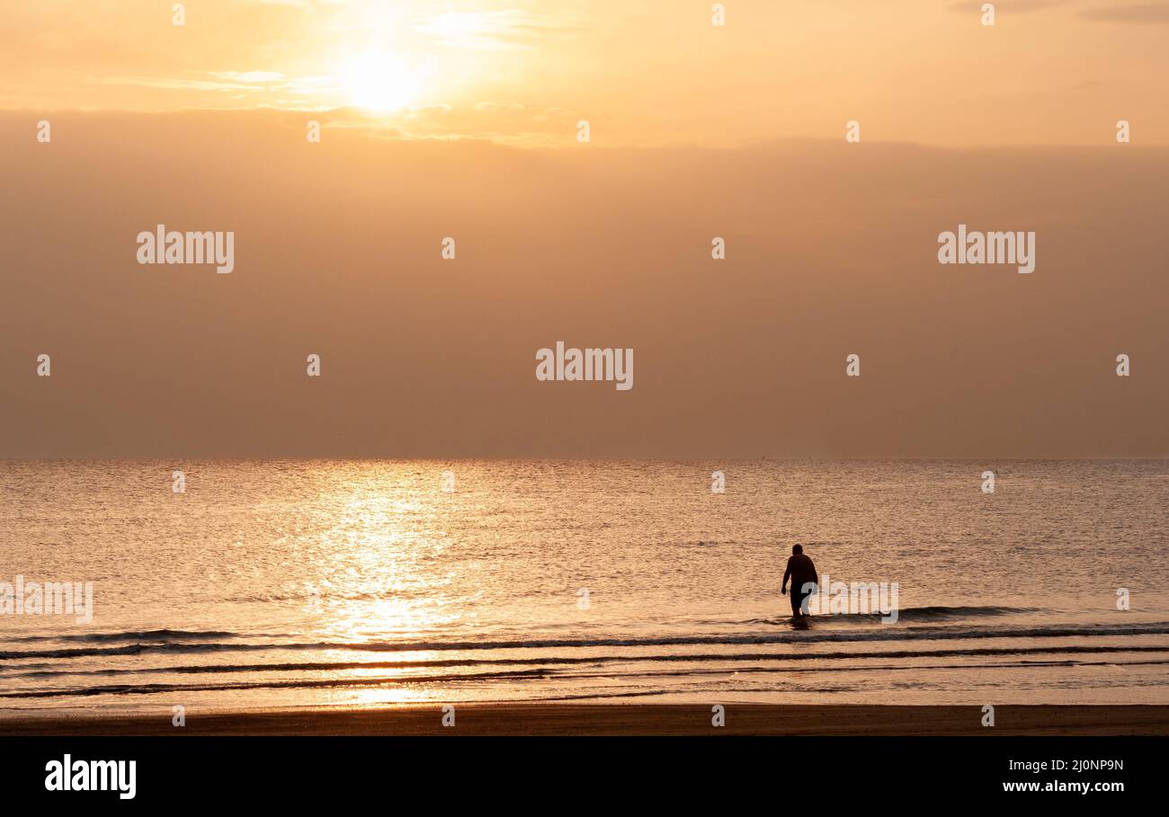 Silhouette d'un homme dans la mer au lever du soleil.Personne non reconnue entrant dans l'océan pour nager le matin. Banque D'Images