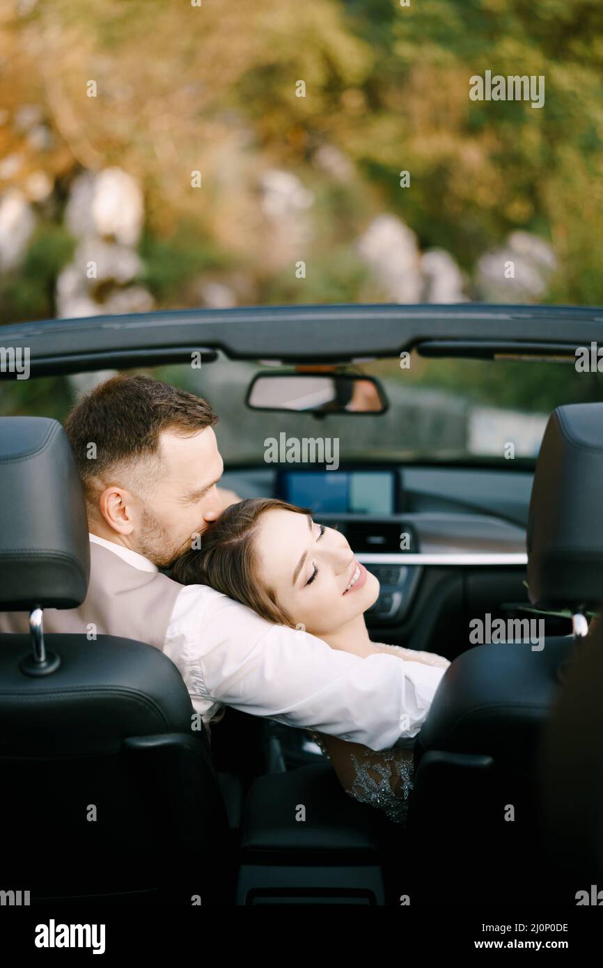 Le marié épouse une mariée qui a posé sa tête sur son épaule dans un convertible Banque D'Images