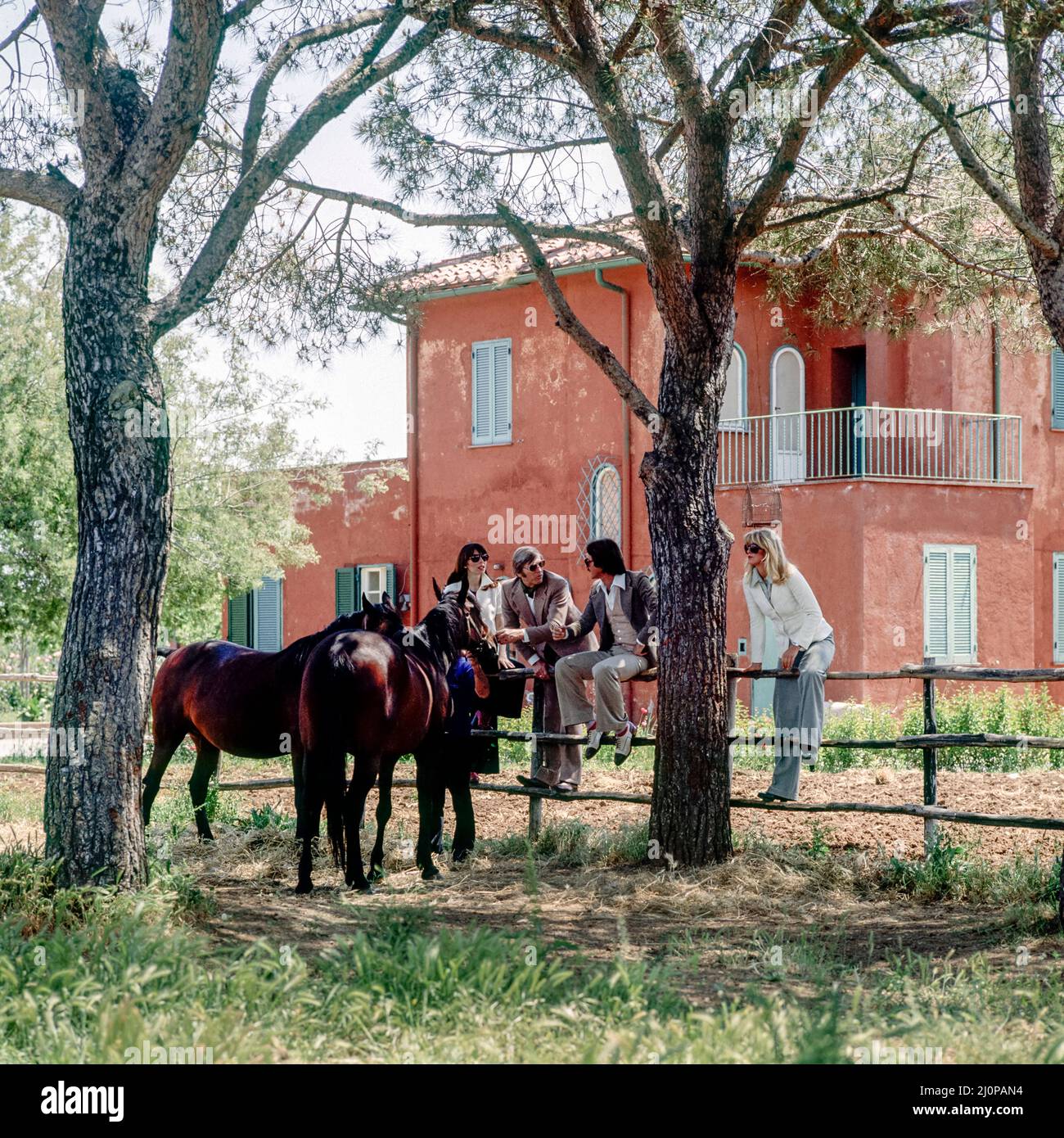 Vintage Italie 1970s, 2 couples d'amis visitent l'élevage de chevaux, assis sur la clôture, la campagne romaine ranch, maison rose, Lazio, Europe, Banque D'Images