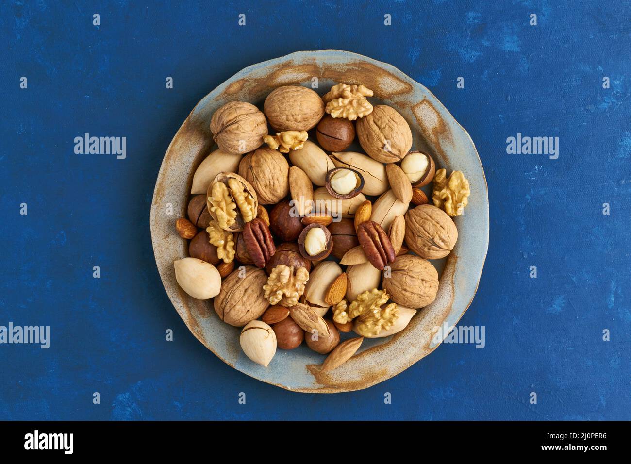 Bleu classique dans la nourriture. Mélange de noix sur l'assiette - noix, amandes, pacanes, macadamia et couteau pour ouvrir la coquille. Nourriture végétalienne saine. Banque D'Images
