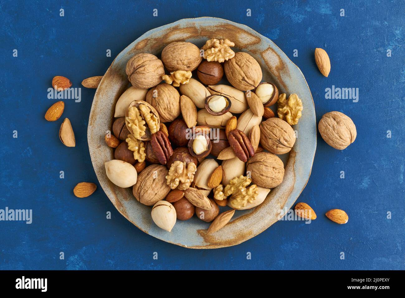 Bleu classique dans la nourriture. Mélange de noix sur l'assiette - noix, amandes, pacanes, macadamia et couteau pour ouvrir la coquille. Nourriture végétalienne saine. Banque D'Images