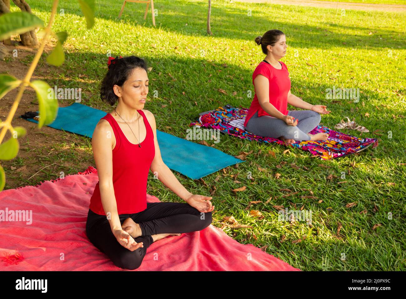Goias, Brésil – 11 mars 2022 : cours de yoga dans un parc public de la ville. Deux personnes pratiquant le yoga dans un parc herbacé bordé d'arbres. Banque D'Images