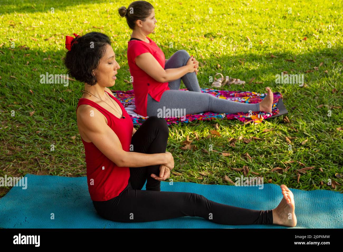 Goias, Brésil – 11 mars 2022 : cours de yoga dans un parc public de la ville. Deux personnes pratiquant le yoga dans un parc herbacé bordé d'arbres. Banque D'Images