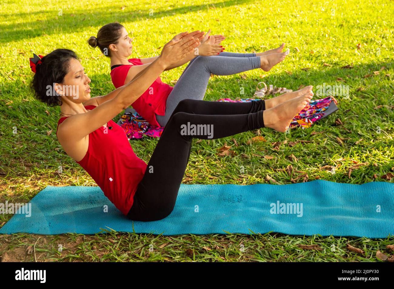 Goias, Brésil – 11 mars 2022 : cours de yoga dans un parc public de la ville. Deux personnes pratiquant le yoga dans un parc herbacé bordé d'arbres. Banque D'Images