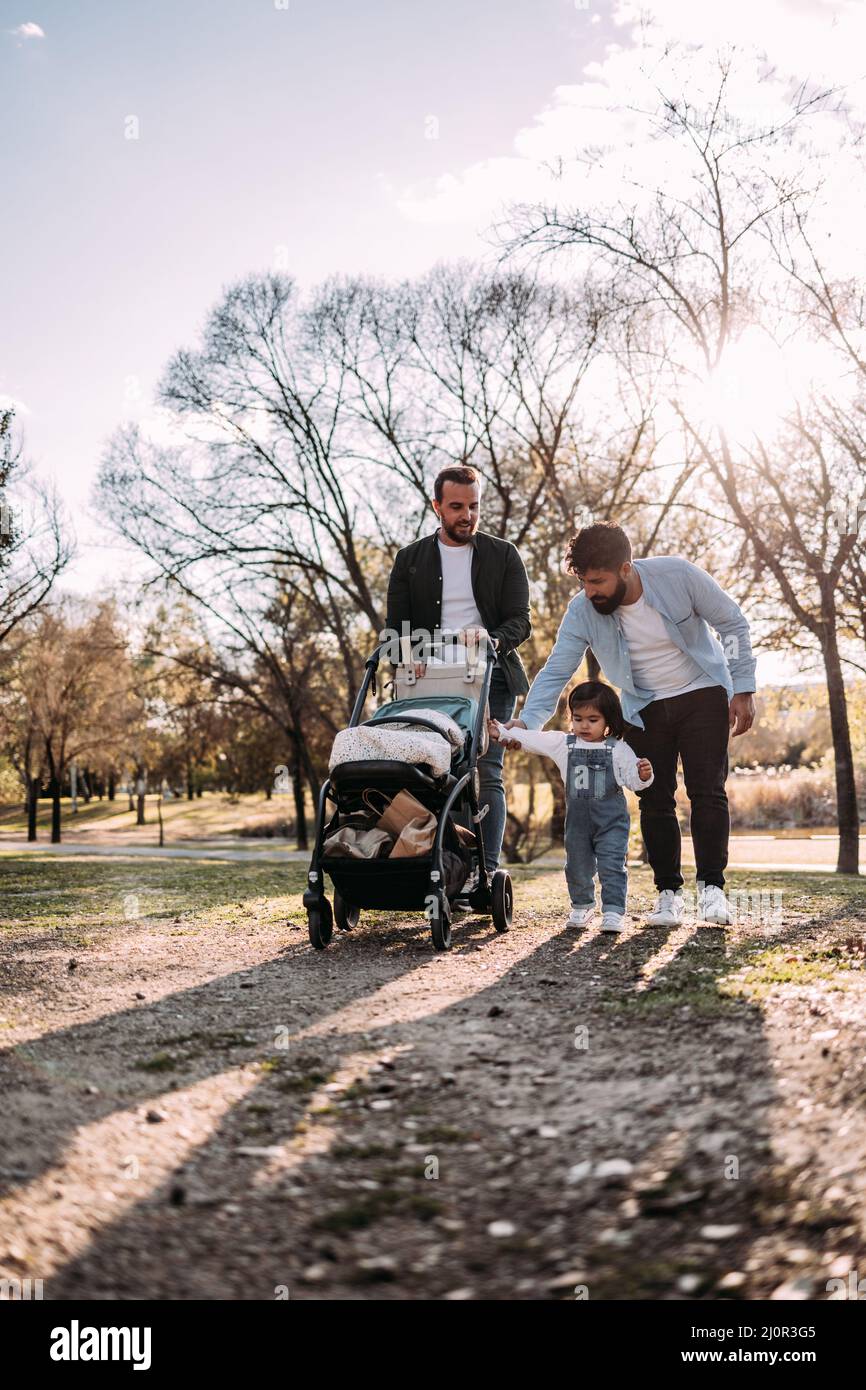 Couple gay multiethnique de sexe masculin marchant avec leur petite fille dans le parc. Concept de famille moderne. Verticale Banque D'Images