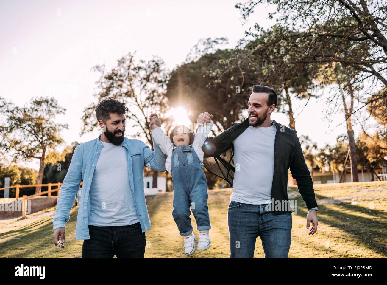 Un couple gay masculin lève leur petite fille qui rit avec joie. Concept de famille moderne et varié. Banque D'Images