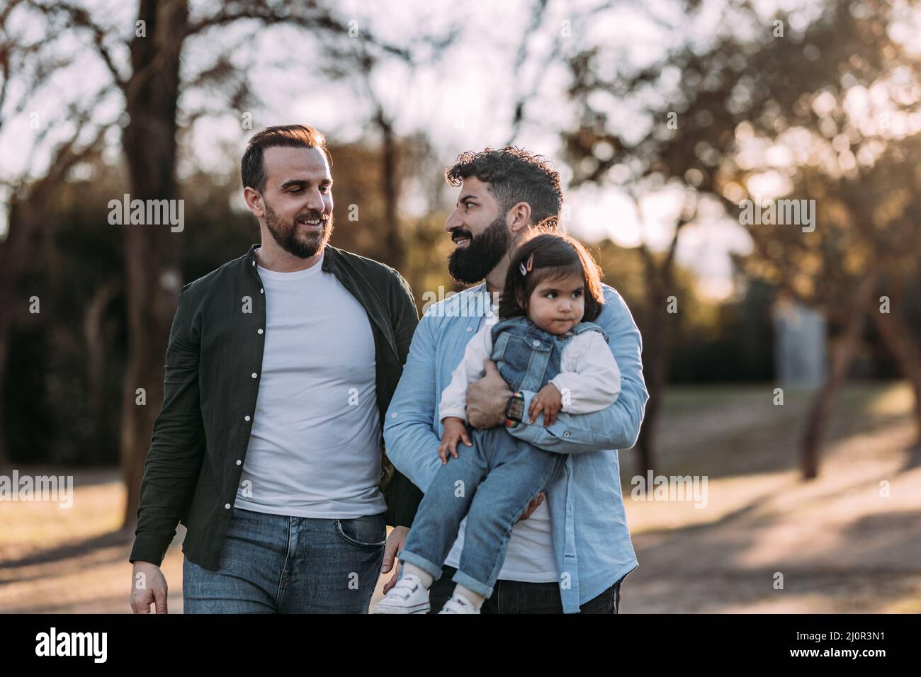 Un couple gay masculin se promette dans le parc amoureux de leur fille dans les bras. Banque D'Images