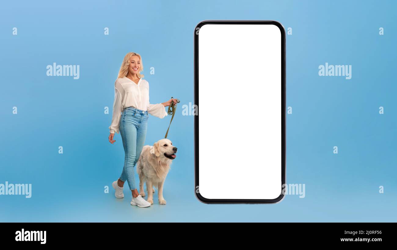 Jeune femme marchant son chien près d'un grand smartphone Banque D'Images