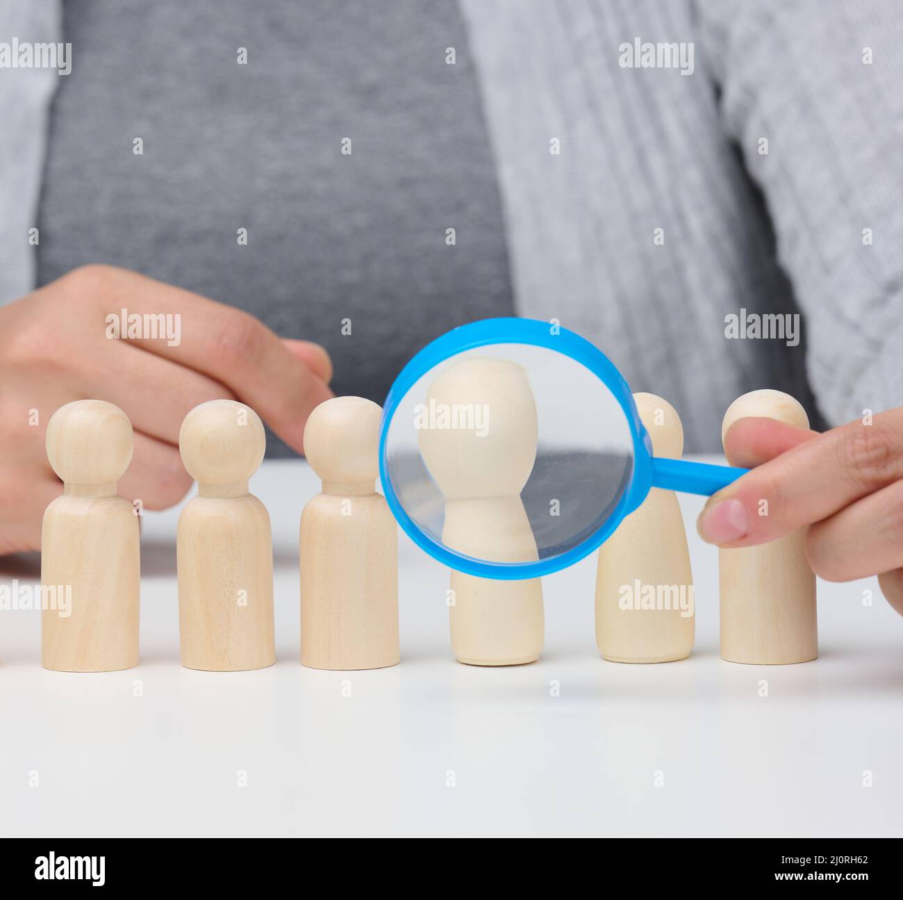 Figurines d'hommes sur une table blanche, une main femelle tient une loupe sur une. Concept de recherche d'employés dans la co Banque D'Images