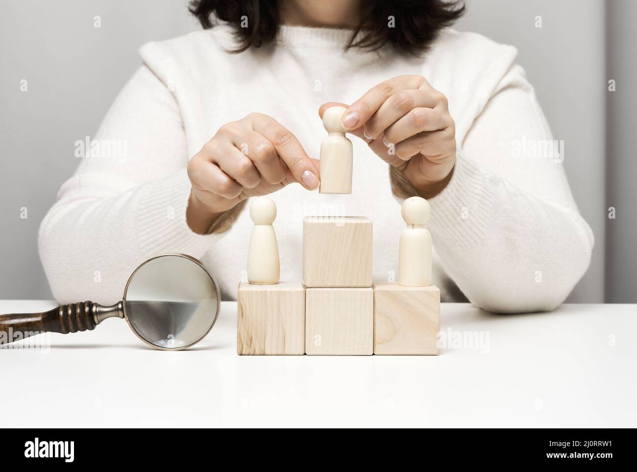 Une femme dans un chandail blanc met une figurine en bois sur le podium. Le concept de la recherche d'employés, de l'avancement professionnel. Em. Talentueux Banque D'Images