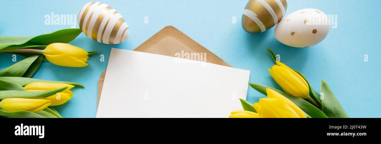 Bannière Pâques salutations: Tulipes jaunes, oeufs dorés et blancs sur fond bleu. Une lettre avec un espace de copie. Vacances de printemps. Banque D'Images