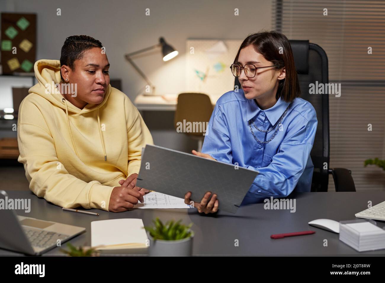 Portrait de deux jeunes femmes discutant de la documentation tout en travaillant tard la nuit au bureau Banque D'Images