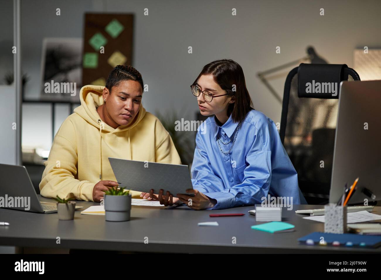 Portrait de deux jeunes femmes discutant de la documentation tout en travaillant tard dans la nuit au bureau Banque D'Images